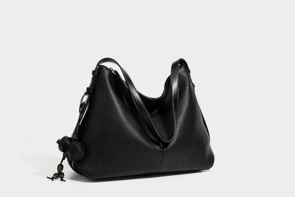 Slouchy hobo shoulder bag with pebbled leather-look finish, zip-top closure, gold-tone hardware, and hanging bead charm
