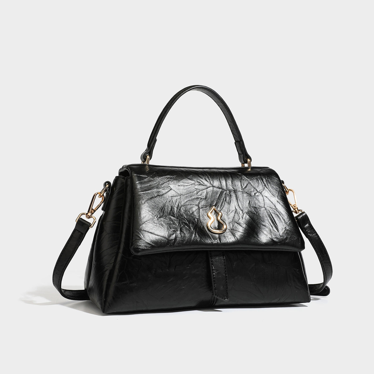 Structured black satchel bag with glossy crinkled leather-look finish, gold-tone emblem flap closure, slim top handle, and
