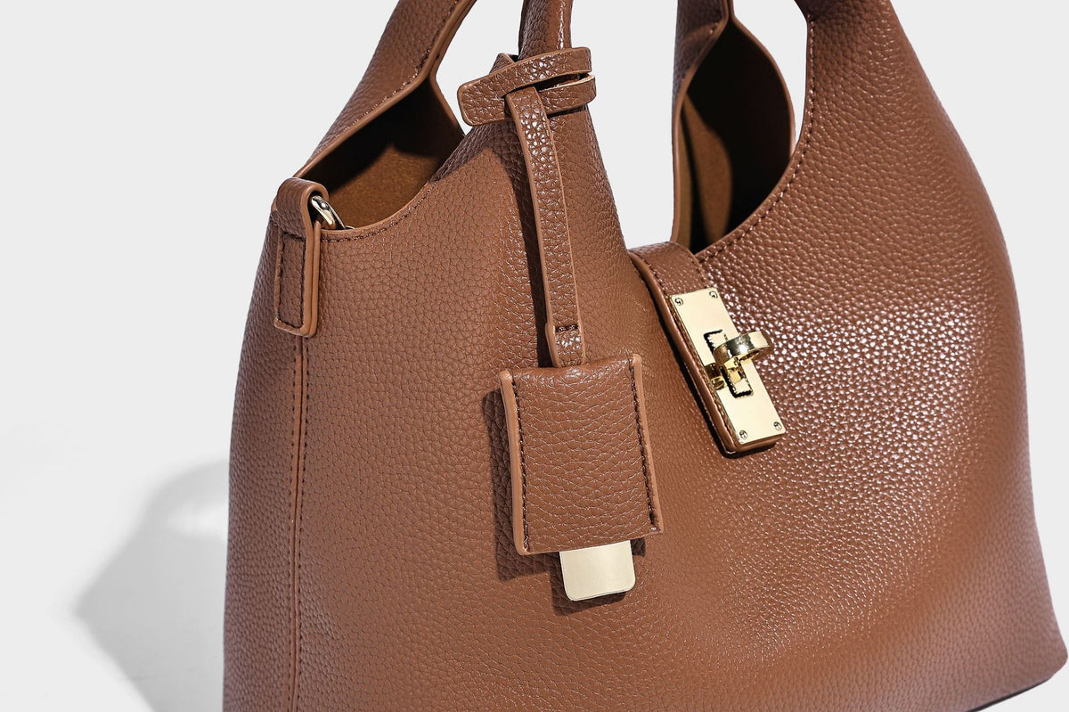 Structured pebbled-texture bucket bag with arched top handles, gold-tone turn-lock closure, and detachable shoulder strap