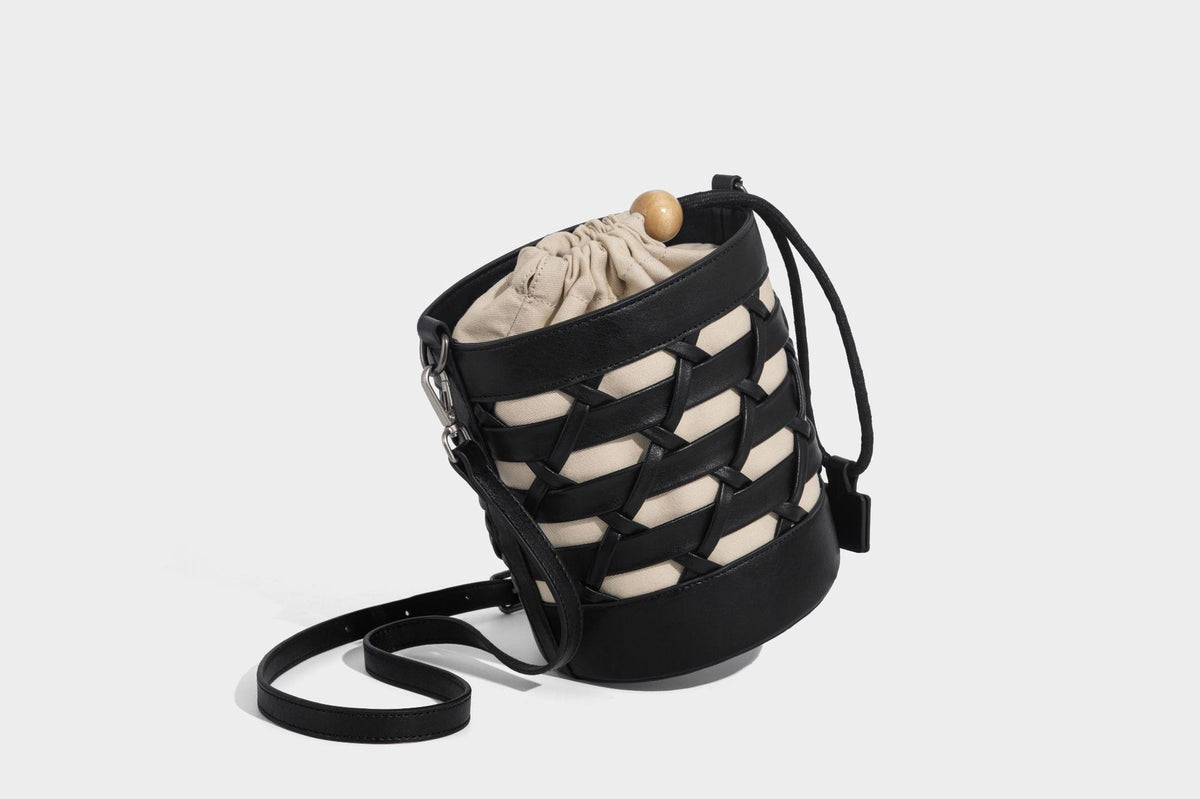 Small cylindrical woven lattice bucket bag with leather-look black trim, beige canvas body, wooden bead drawstring closure