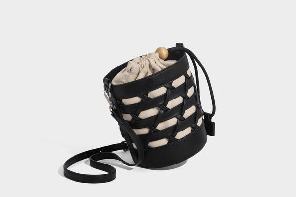 Small cylindrical woven lattice bucket bag with leather-look black trim, beige canvas body, wooden bead drawstring closure