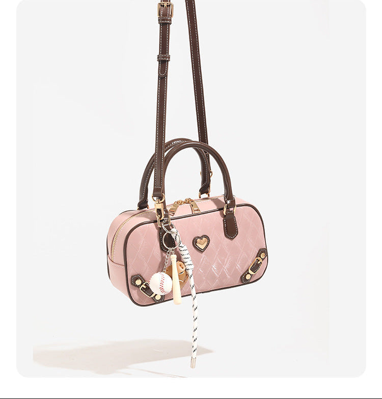 Blush pink quilted bowling barrel bag with dark brown leather-look trim and handles, baseball bat and ball charm, gold-tone