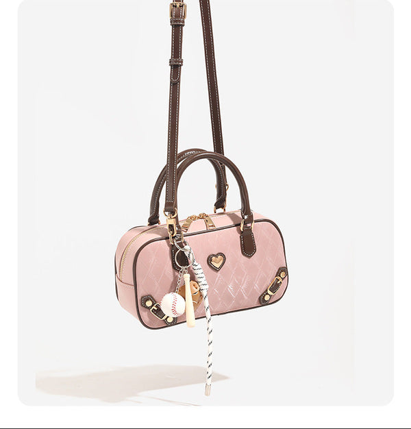 Blush pink quilted bowling barrel bag with dark brown leather-look trim and handles, baseball bat and ball charm, gold-tone