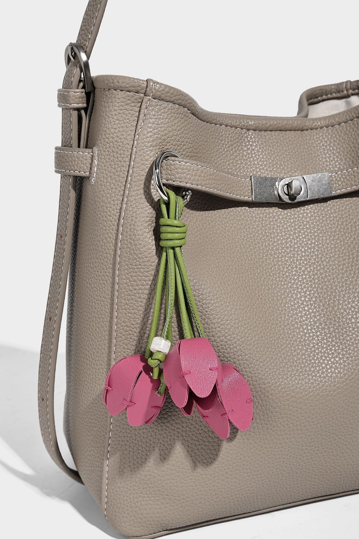 Soft-structured pebbled bucket shoulder bag with front turn-lock strap detail, adjustable strap, and hanging floral tassel