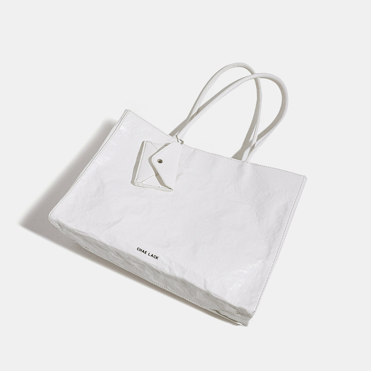 Structured rectangular crinkle leather-look tote bag with long rounded handles, zip top, and envelope-style hanging tag