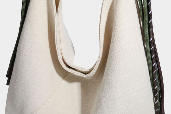 Soft slouchy cream canvas shoulder tote with braided brown and green cord handle, gold-tone ring hardware, and tassel trim