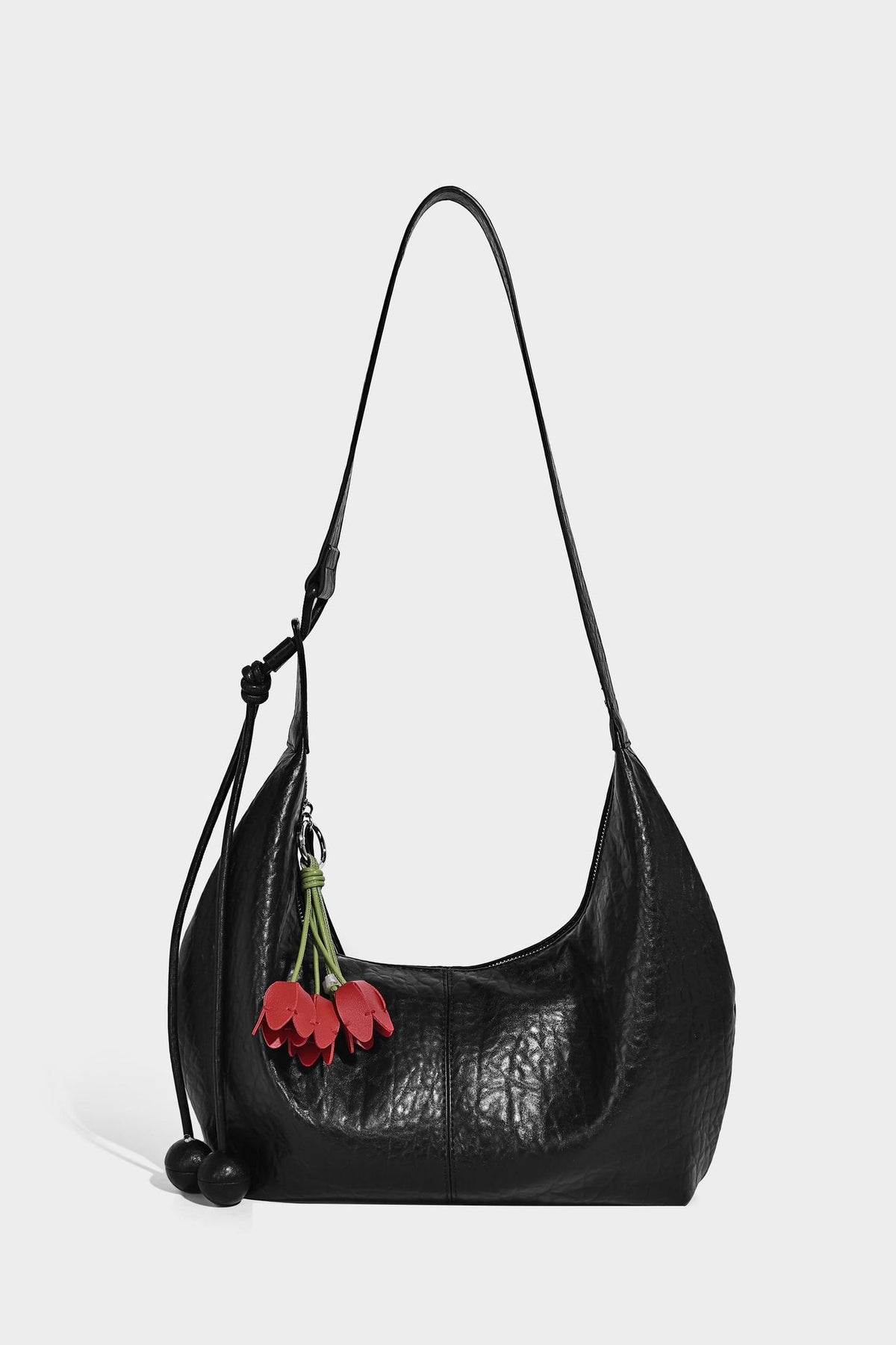 Slouchy crescent half-moon shoulder bag in pink pebbled textured finish with floral charm and knotted side detail, detail