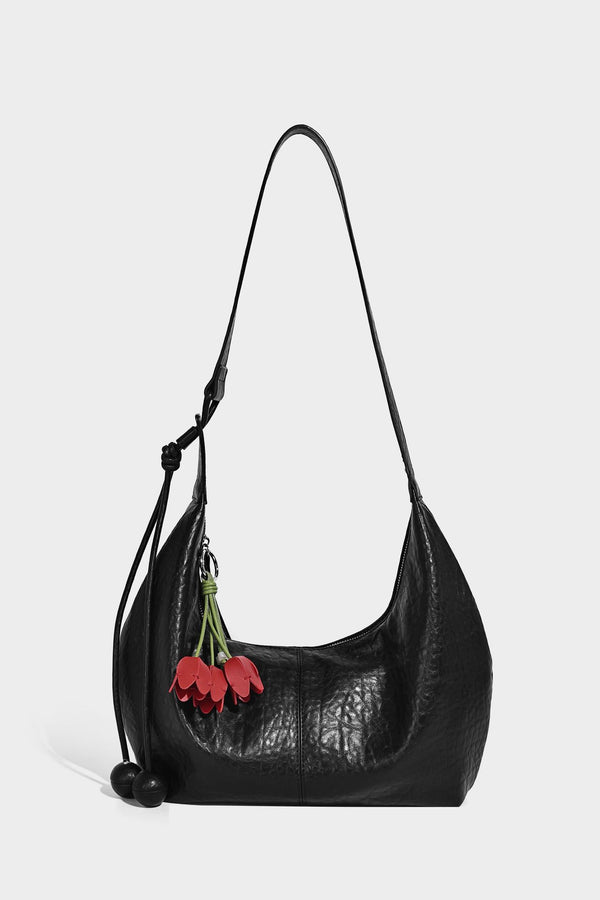 Slouchy crescent half-moon shoulder bag in pink pebbled textured finish with floral charm and knotted side detail, detail
