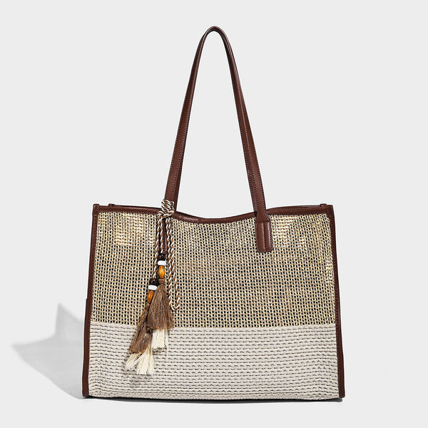 Two-tone woven straw tote bag with leather-look brown trim, long shoulder straps, and knotted tassel charm, front view