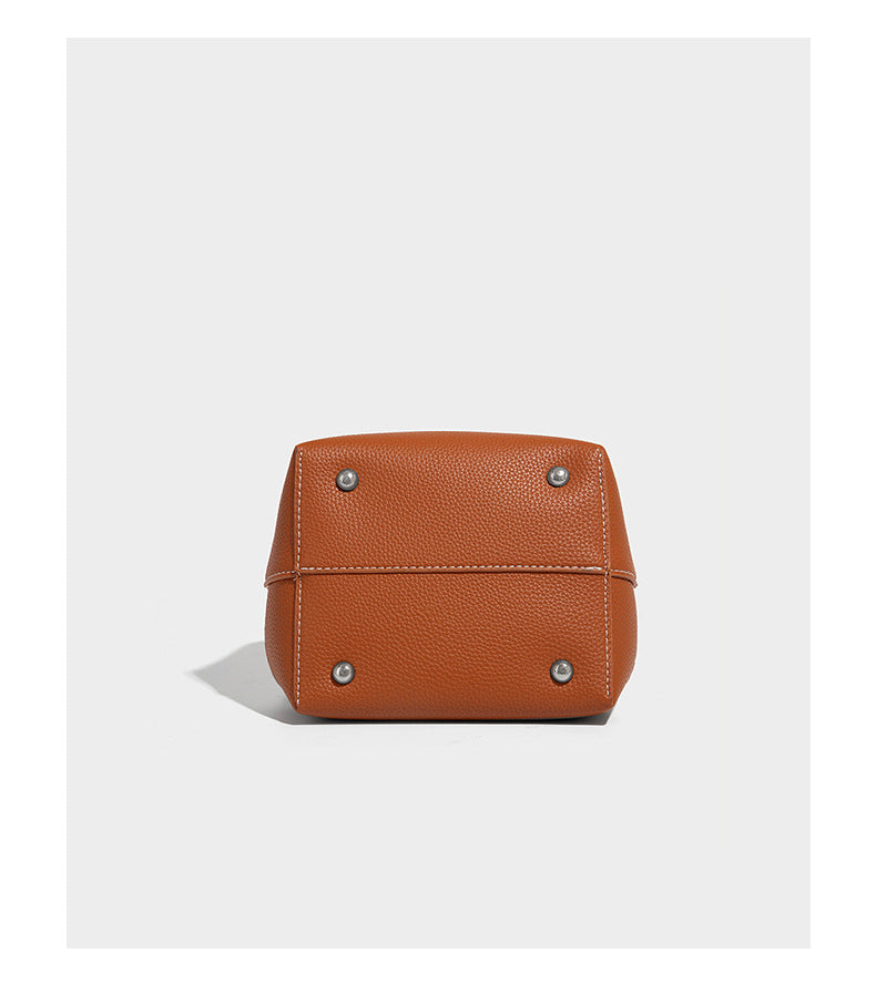 Small two-tone pebbled drawstring bucket bag with tan contrast base, metal toggle hardware, short top handle, and detachable