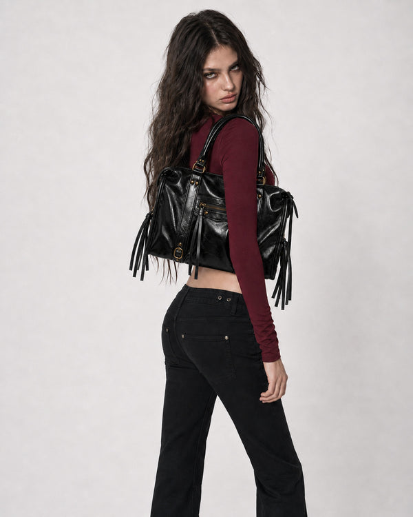 Structured glossy leather-look satchel bag with brass-tone studs, side tassel fringe, dual top handles, and front zip pocket