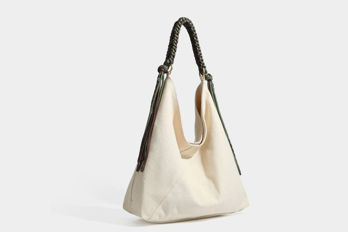 Soft slouchy cream canvas shoulder tote with braided brown and green cord handle, gold-tone ring hardware, and tassel trim