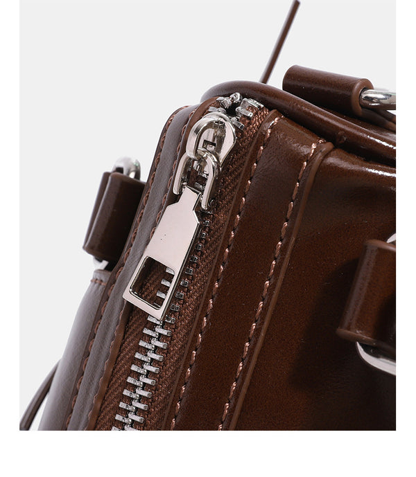 Kleine, formstabile Glanzledertasche mit zwei Henkeln, vorderer Klappentasche, herzförmigem Charm-Verschluss und silberfarbenem