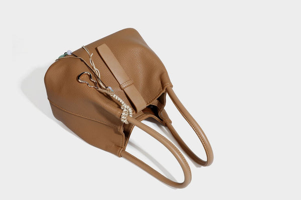 Pebbled leather-look bucket tote bag with rolled double handles, drawstring closure, braided cord charm, and detachable