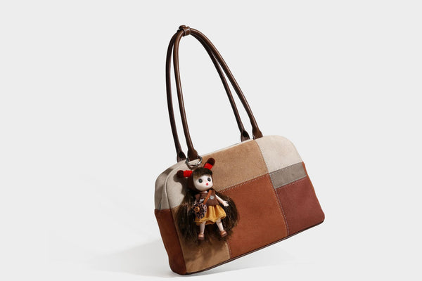 Boxy patchwork suede-look shoulder tote in tan, beige, rust, and brown panels with double brown straps and hanging doll