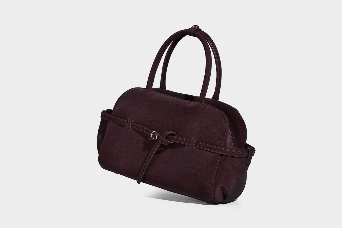 Strukturierte Henkeltasche aus mattem, genarbtem Material mit umlaufendem Riemen und Ringbeschlägen, zwei oberen Tragegriffen und abnehmbarem Crossbody-Riemen