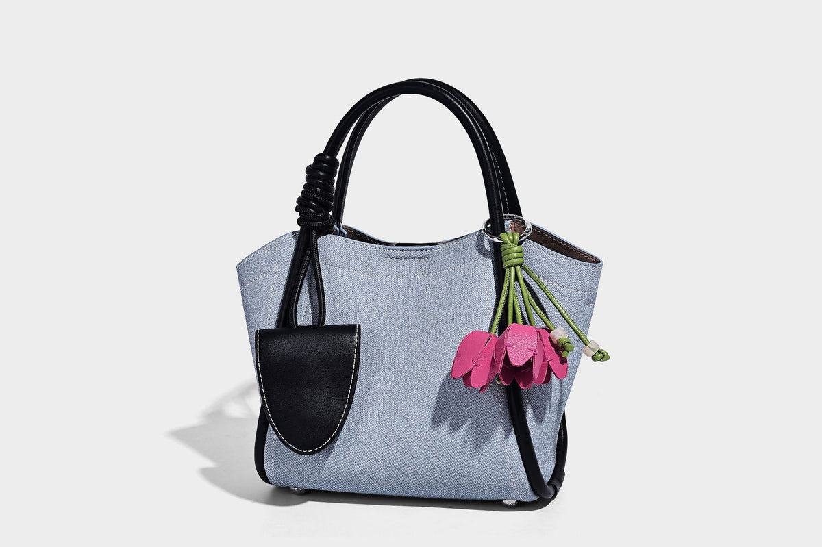 Light blue denim trapezoid tote bag with black leather-look trim, knotted top handles, detachable crossbody strap, front