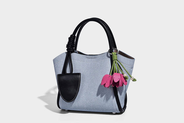 Light blue denim trapezoid tote bag with black leather-look trim, knotted top handles, detachable crossbody strap, front
