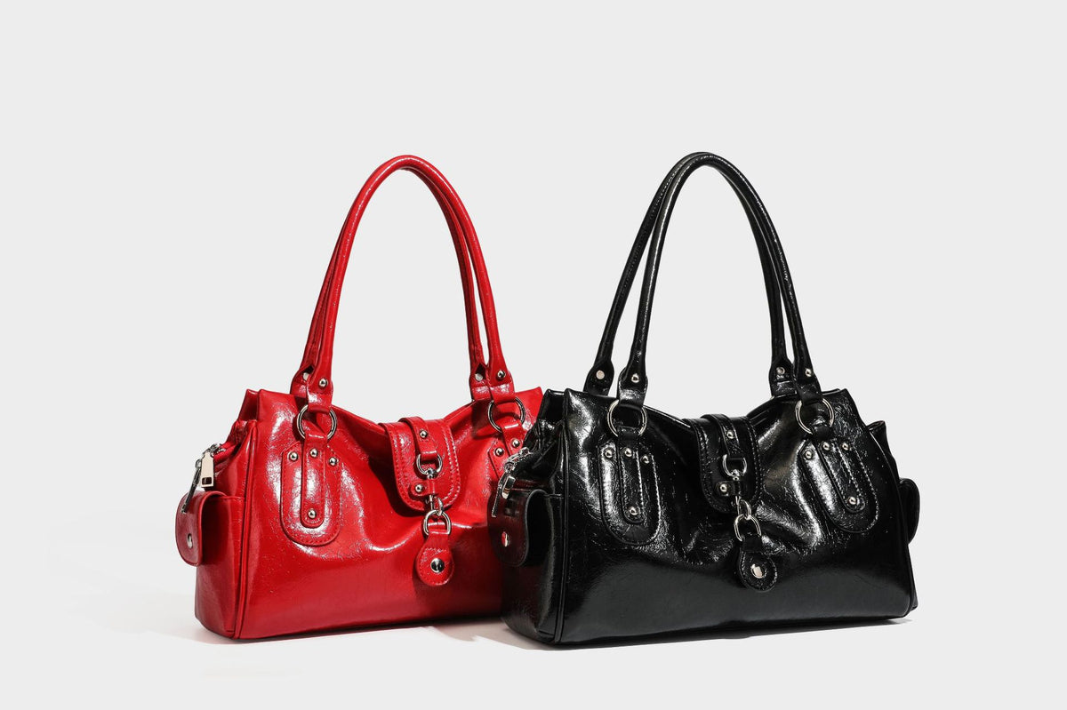 Glänzende, geknautschte Barrel-Satchel mit zwei oberen Tragegriffen, vorderem Klappen-Riemen-Panel, Ring- und Nietenbeschlägen sowie einem abnehmbaren