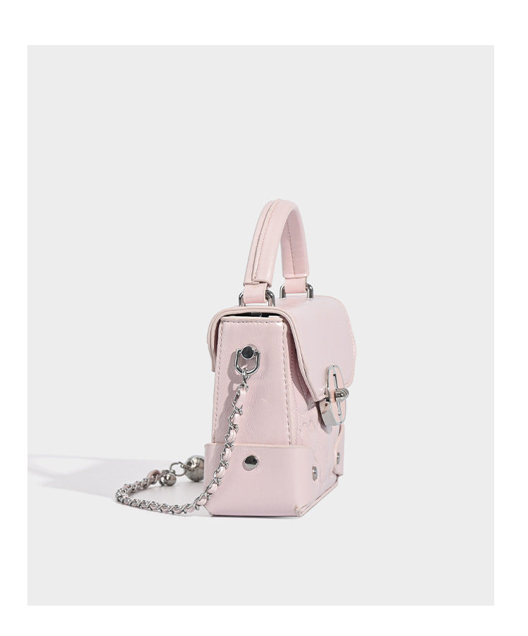 Kleine strukturierte Box-Tasche aus herzförmig gestepptem PU mit Henkel, silberfarbenem Kettenriemen zum Tragen als Crossbody und ovalem Drehverschluss, Detailansicht