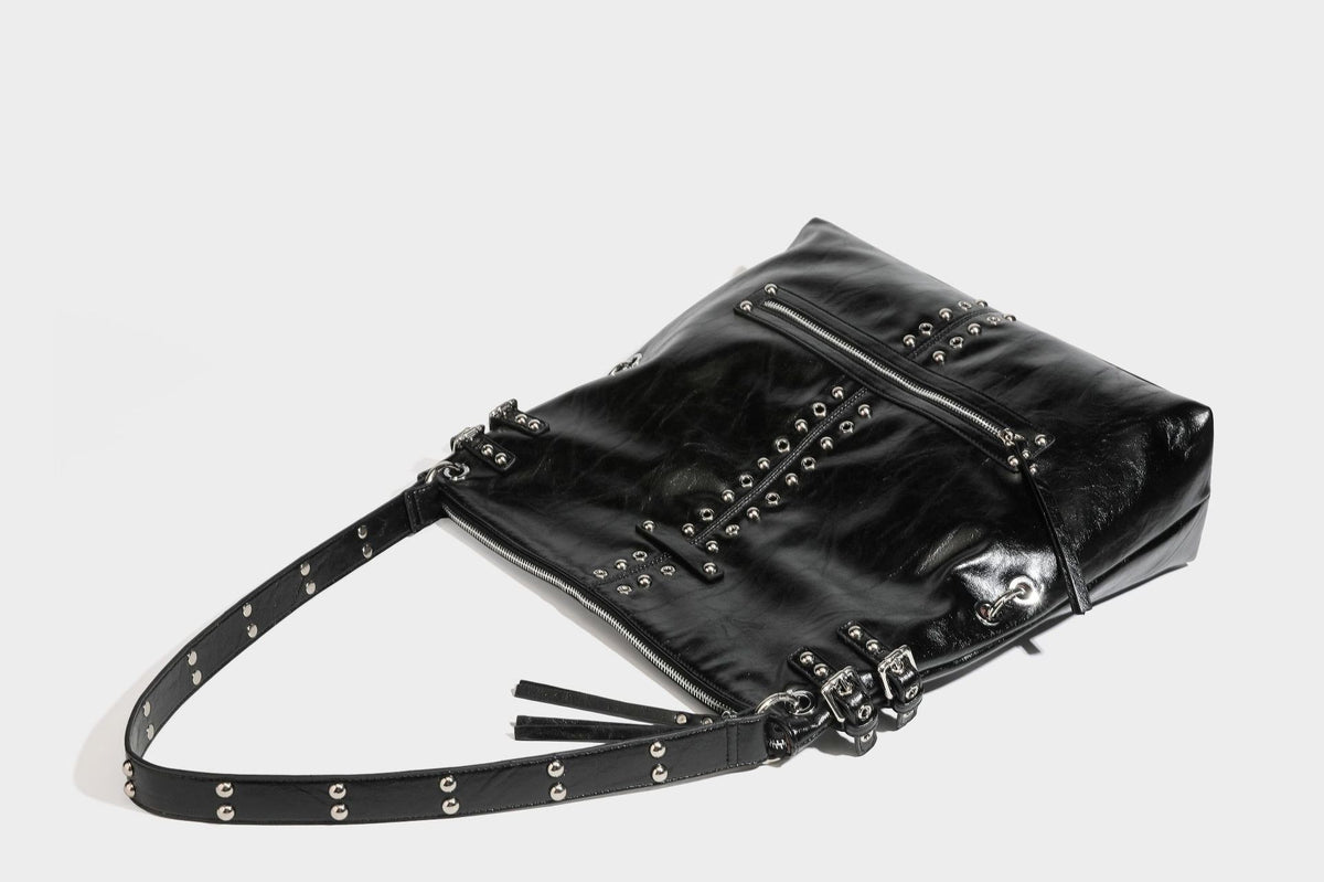 Black glossy leather-look slouchy shoulder bag with silver stud and eyelet hardware, top zip closure, front zip pocket, and