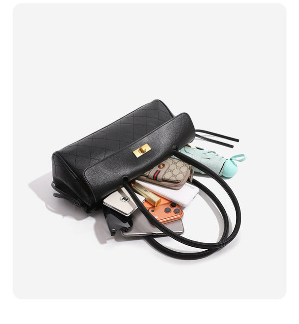 Structured black baguette bag with diamond-quilted front panel, gold-tone turn-lock flap closure, and dual looped top