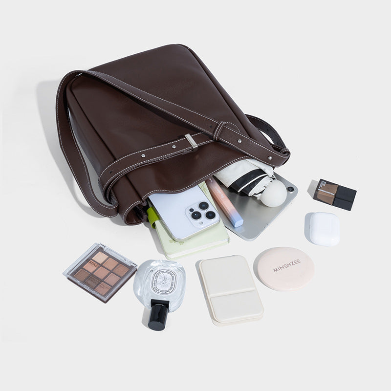 Structured dark brown leather-look bucket bag with white contrast stitching, front wraparound belt buckle strap, and long
