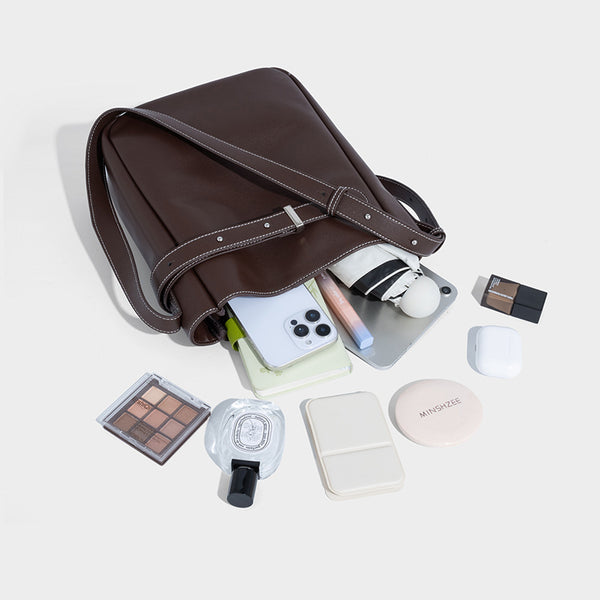 Structured dark brown leather-look bucket bag with white contrast stitching, front wraparound belt buckle strap, and long