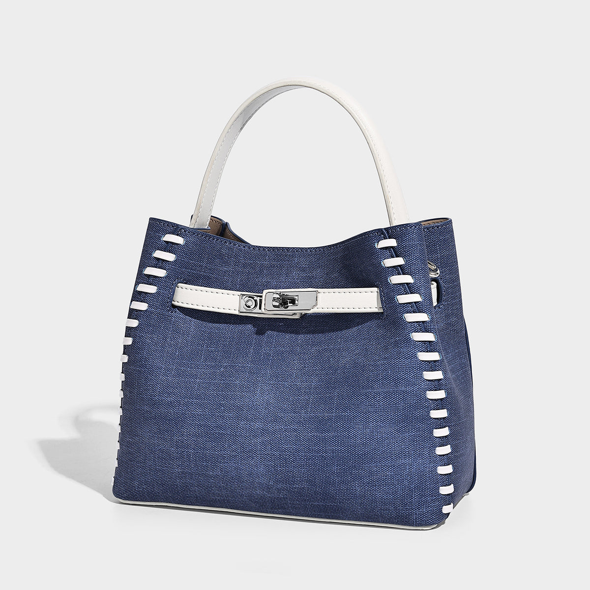 Structured denim bucket bag with white whipstitch trim, silver turn-lock hardware, short top handles, and a long adjustable