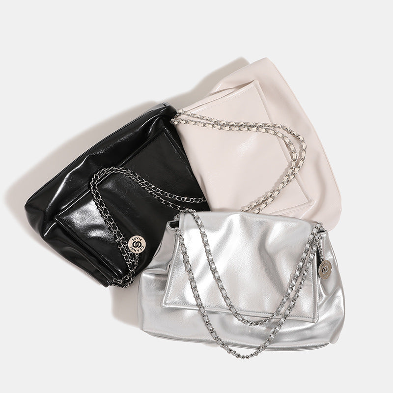 Soft trapezoidal chain-strap shoulder bag with foldover flap and circular logo medallion, detail view 4