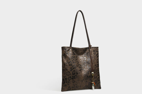 Large leopard print shoulder tote bag in tan and brown with slim dark straps and dangling beaded charm hardware, detail view