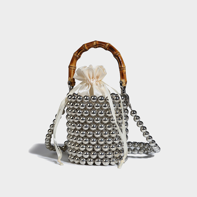 Small cylindrical bucket bag with glossy faux-pearl bead exterior, bamboo arched top handle, satin drawstring closure, and