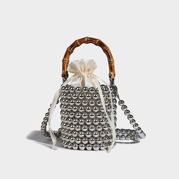 Small cylindrical bucket bag with glossy faux-pearl bead exterior, bamboo arched top handle, satin drawstring closure, and