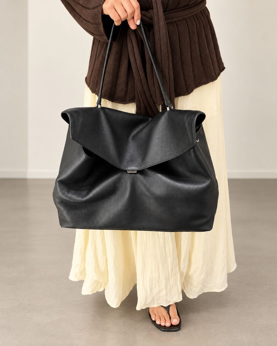 Large black slouchy leather-look shoulder bag with V-shaped envelope flap, silver-tone clasp, and adjustable strap, detail
