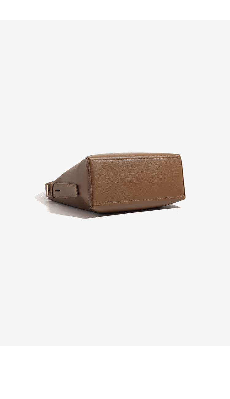 Structured smooth leather-look bucket shoulder bag with long adjustable strap and gold-tone buckle hardware in brown, detail