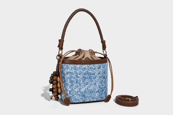 Small light blue woven bucket bag with brown leather-look trim, braided top handle, brass-tone ring hardware, drawstring