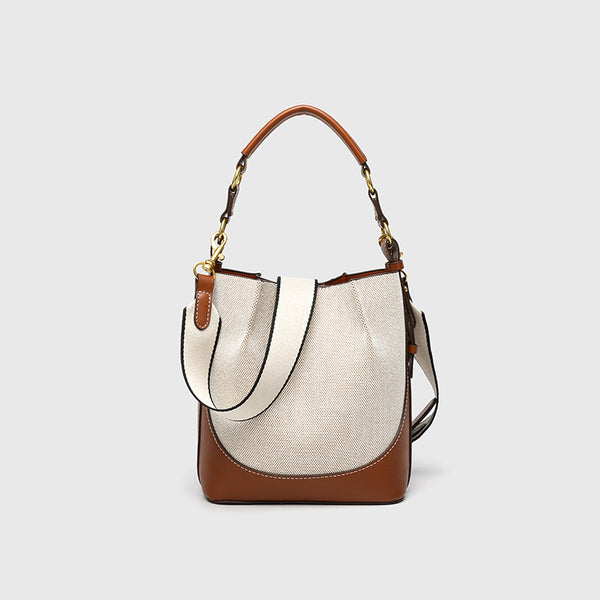 Cream canvas and tan leather-look bucket bag with arched top handle, wide detachable shoulder strap, and gold-tone hardware