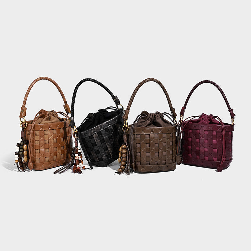 Small woven check-panel bucket bag with braided top handle, drawstring closure, bead charm, and detachable shoulder strap