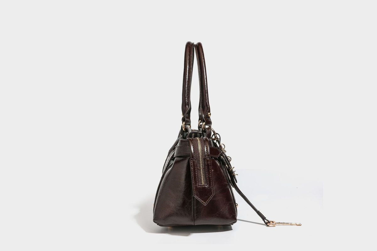 Glossy dark brown structured Boston satchel with heart-shaped lock charm, star pendant, rivet studs, multi-strap front panel