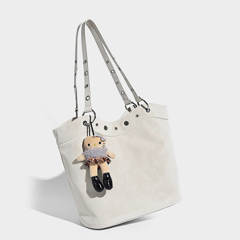 Große matte Tote-Bag in Lederoptik mit silberfarbenem Ösenbesatz, zwei Schulterriemen und abnehmbarem Plüschpuppen-Anhänger, Detailansicht