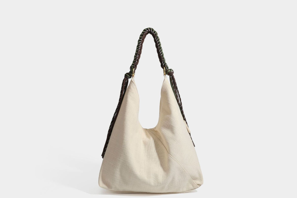 Soft slouchy cream canvas shoulder tote with braided brown and green cord handle, gold-tone ring hardware, and tassel trim