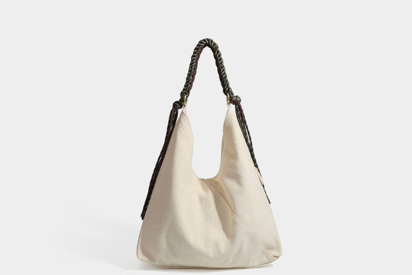 Soft slouchy cream canvas shoulder tote with braided brown and green cord handle, gold-tone ring hardware, and tassel trim