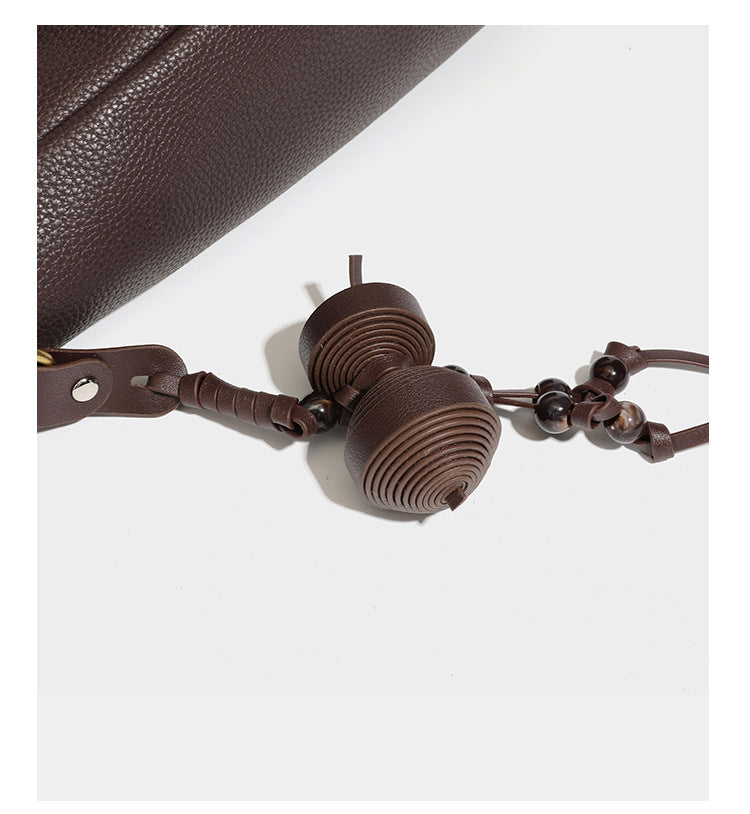 Hobo-Schultertasche in dunklem Espresso mit genarbter Oberfläche, warmen cognacfarbenen Details, verstellbarem schmalem Riemen, goldfarbenen Ringbeschlägen und geknotetem