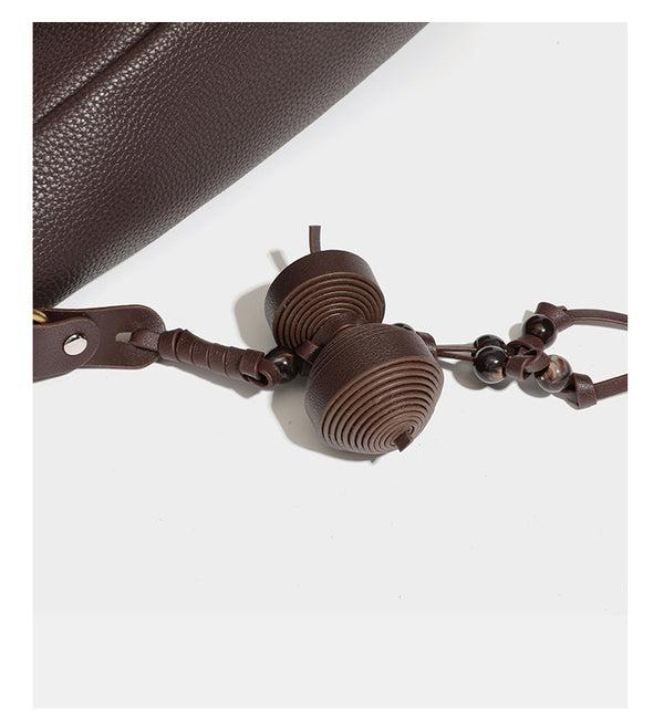 Hobo-Schultertasche in dunklem Espresso mit genarbter Oberfläche, warmen cognacfarbenen Details, verstellbarem schmalem Riemen, goldfarbenen Ringbeschlägen und geknotetem