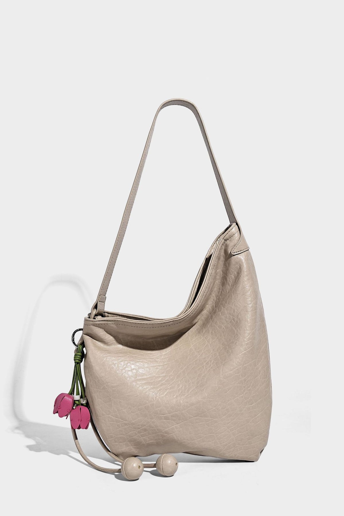 Slouchy hobo shoulder bag in pale yellow with slim strap, drawstring bead closure, and pink tulip floral charm, detail view