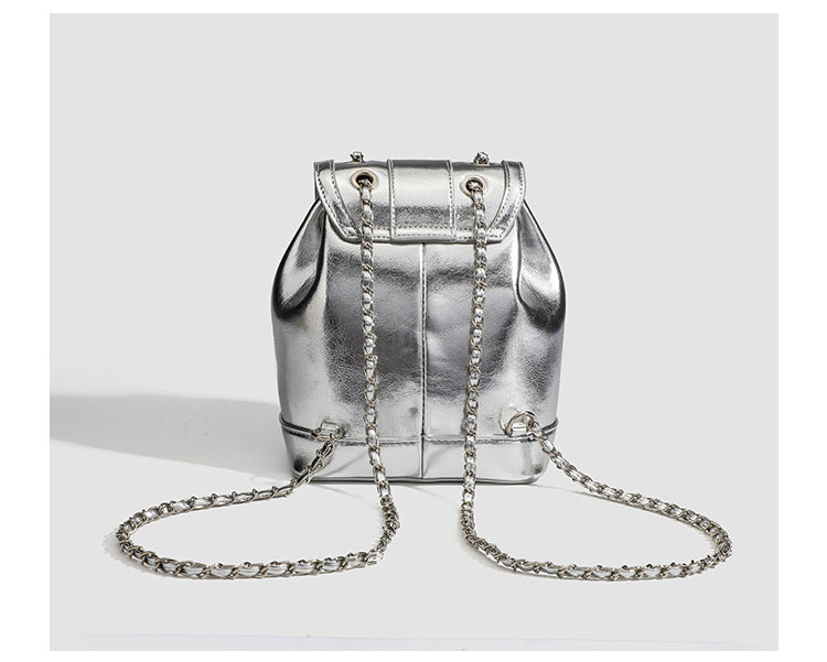 Kompakter Rucksack in Silbermetallic mit mehrfarbigen Kristallnieten, runder Klappe mit Drehverschluss und ineinander verflochtenem Silber
