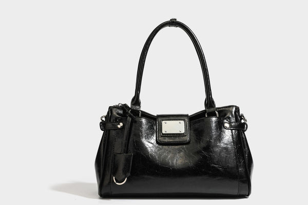 Structured glossy crinkled leather-look satchel with double top handles, front metal-plaque tab, silver-tone hardware, and