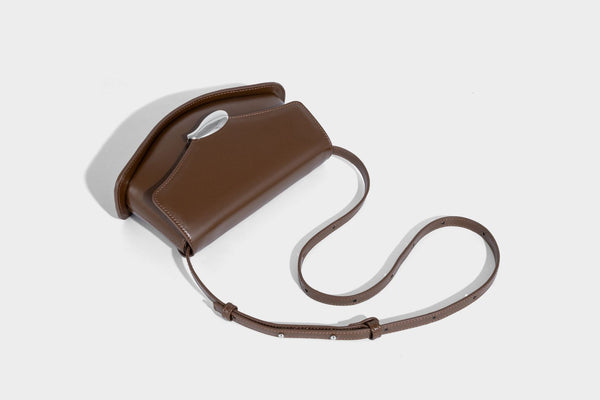 Small structured saddle bag with glossy leather-look finish, angular flap front, silver-tone metal clasp, and slim