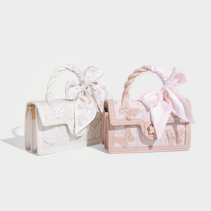 Small structured white flap bag with butterfly embroidery, flower-shaped turn-lock clasp, braided top handle with scarf bow
