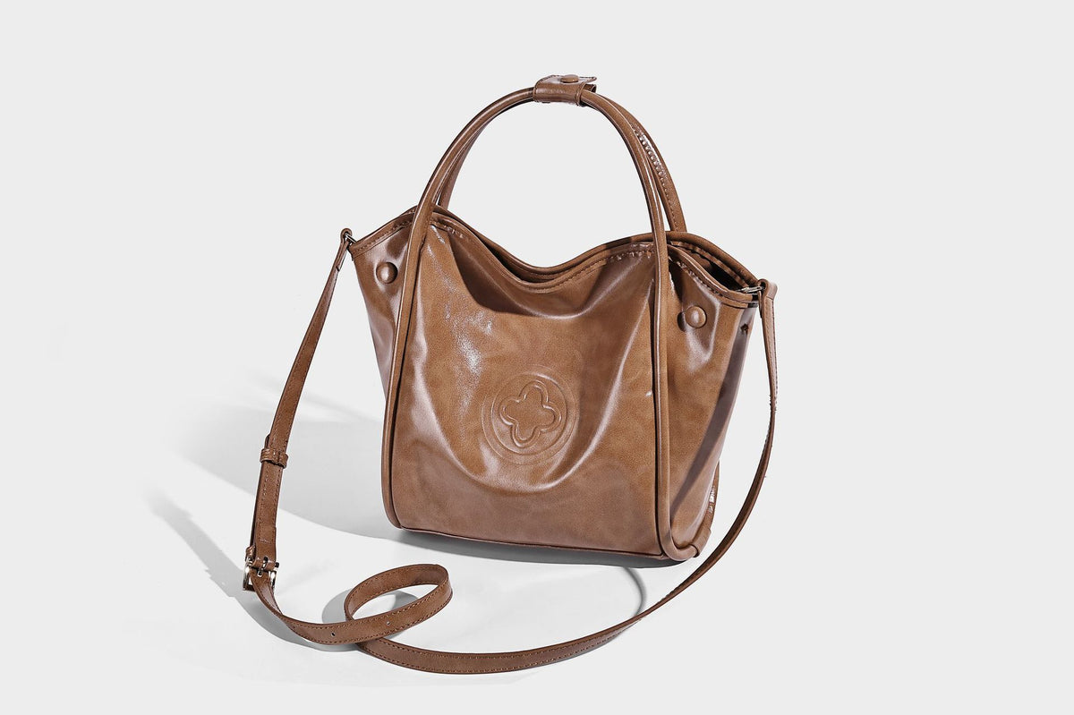 Glossy leather-look structured tote bag with rounded top handles, detachable shoulder strap, embossed front emblem, and side